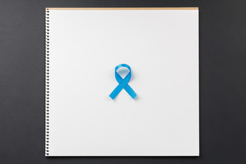 blue cancer ribbon on notebook lying on dark table