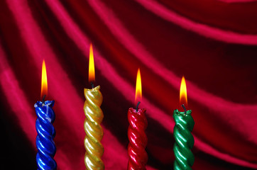 Four burning colored candles on the background of burgundy drapery.