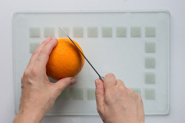 Woman hand cut orange with knife on white background