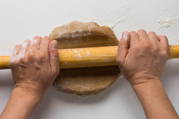 Woman hands rolling out gingerbread dough by rolling pin on white background