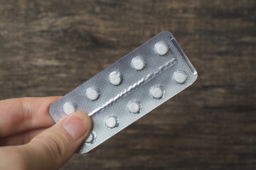 White pills blister hand holding over wood background, painkiller, sedative, antibiotic or drug...