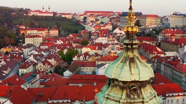 Aerial view St. Nicholas church and mala strana district at morning. Drone flying at low above dome of famous cathedral, moving up near spire decorated masonic symbol. Cityscape Prague at sunrise