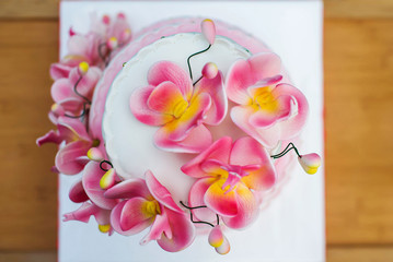 Large white-pink holiday cake decorated with flowers on a wooden table close-up. View from above.