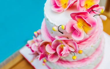 A large pink and white holiday cake decorated with flowers on a wooden tray on the street against the background of water. Copy space