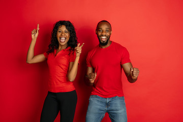 Young emotional african-american man and woman in bright casual clothes posing on red background....