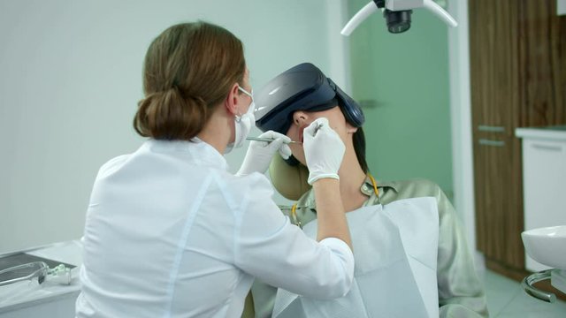 Dentist works, girl sits with virtual reality glasses
