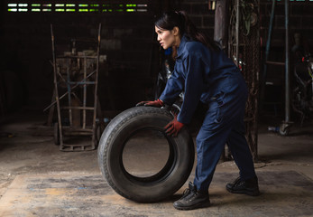 Female auto repair mechanic pushing vehicle tyre in garage workshop - Asian car care maintenance technician replacing tire on customer truck - Service industry, repair shop and automotive concept