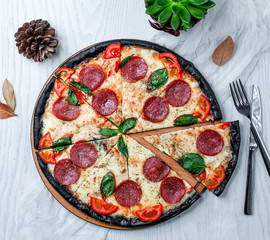 black pepperoni pizza with tomato and basil