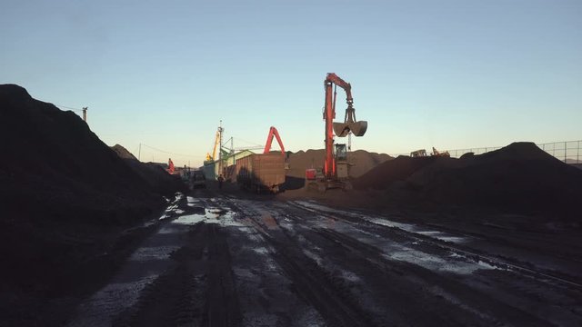 Overall plan. The territory of the marine coal terminal. An excavator with a large bucket works among coal heaps.