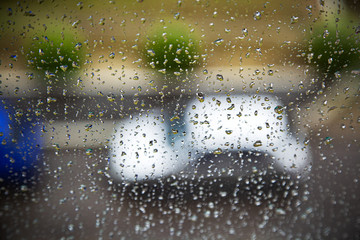 Natural picture of raindrops on a window with a car on a blurred background. Texture background with wet drops of water on a glass and a car outside the window. Autumn rainy weather.