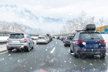 Fototapeta na wymiar Winter highway with many different cars stucked in traffic jam due ti bad weather conditions. Vehicles on road during heavy snowstorm and blizzard on cold winter day in Austria near Germany border