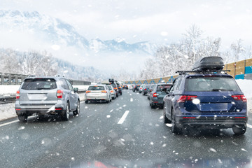 Winter highway with many different cars stucked in traffic jam due ti bad weather conditions. Vehicles on road during heavy snowstorm and blizzard on cold winter day in Austria near Germany border
