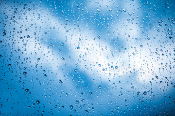 Natural pattern of raindrops on a window with a blue sky with clouds in the background. Textural background with wet drops of water on window.