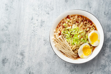 Asian soup ramen with noodles, spring onion, enoki mushrooms and boiled egg in bowl on concrete background. Top view. Copy space.