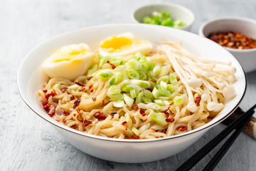 Asian soup ramen with noodles, spring onion, enoki mushrooms and boiled egg in bowl on concrete background. Selective focus.