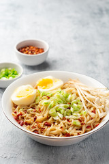 Asian soup ramen with noodles, spring onion, enoki mushrooms and boiled egg in bowl on concrete background. Selective focus.