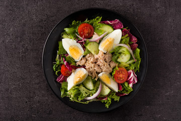 Salad with tuna, egg and vegetables on black background
