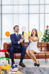 Romantic couples celebrate Christmas on the sofa with happy faces and are fireworks, party poppers to celebrate. Christmas and New Year concept
