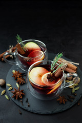 Two cups of Christmas mulled wine or punch with spices and lemon slices on dark wooden background....