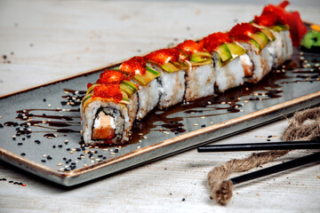 sushi rolls covered with avocado, cream and red tobiko, and soy sauce