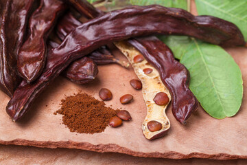 Carob. Organic carob pods with seeds and leaves on tree bark table. Healthy eating, food background.