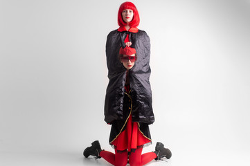 Fashion portrait of devil sexy girl in red tights standing on her knees and embraced by her...