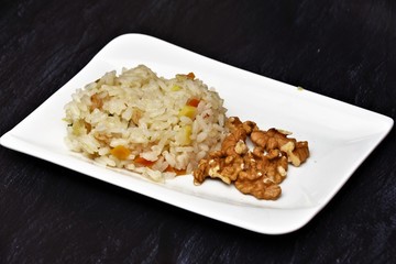 boiled rice with vegetables and walnuts on a white plate on a black table