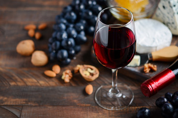 Red wine glass with cheese, grapes, honey and nuts on a wooden table.