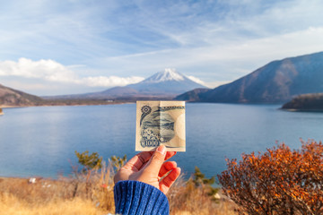 The view of Lake Motoko with a woman's hand holding 1000 yen bank. One of the 5 lakes around Mount Fuji, in the bright blue sky. Japan's landmark, Japan, Fuji san
