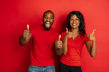 Young emotional african-american man and woman in bright casual clothes posing on red background....