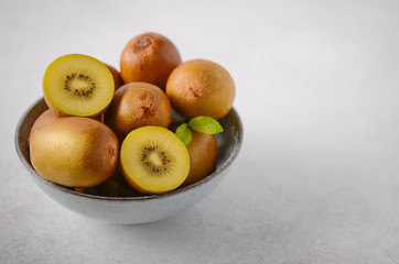 Yellow kiwi fruit in a bowl on a gray concrete background.