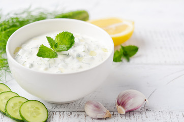 Obraz na płótnie Canvas Greek dip sauce or dressing tzatziki decorated with olive oil and mint on white wooden table.