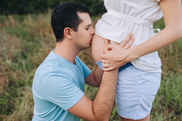 Obraz premium A loving man, husband and father kisses the belly of his beloved pregnant woman and wife. Close-up portrait of a pregnant girl. Expecting a baby. Photography, conception.