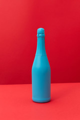 Blue painted spray wine bottle on a duotone red background.