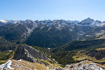 Wild alpine landscape in fall with rocky mountains, forests and some snow under blue sky. Allgau Alps, Tirol, Austria