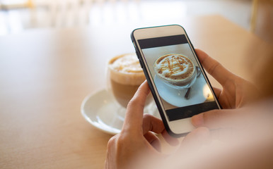The hand of the woman using a smartphone to take a picture of a coffee in a cafe to post on social...