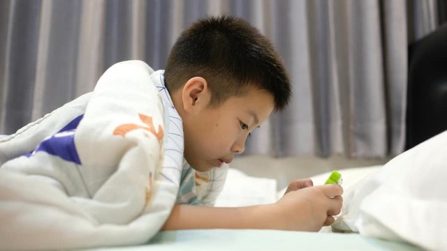 asian chinese boy playing smartphone on bed, kid use phone and play game, addicted game and cartoon, 