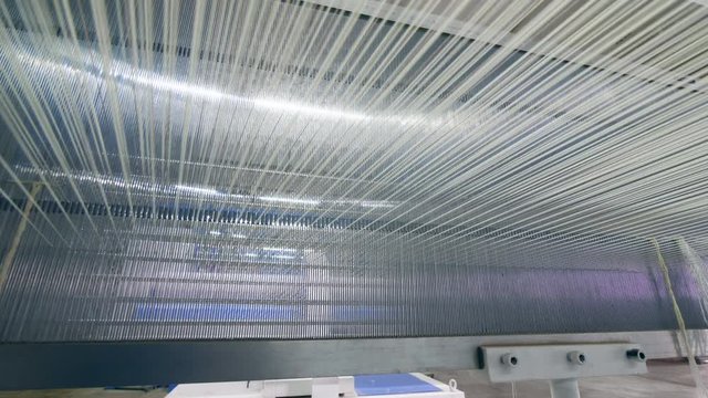 Lots of strings woven on a factory machine automatically. Industrial textile factory.