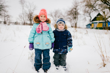 Two funny children posing in snowy field in cold winter day and holding each other hands.