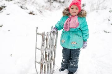 Lovely smiling girl with frozen sled in her hand posing for camera in winter snowy day outdoor.