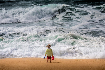 Fototapeta na wymiar Baby with sandbox bucket and shovel toys watching storm and windy ocean