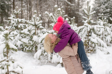 Happy mother holding her daughter above her head and having fun in winter snowy forest
