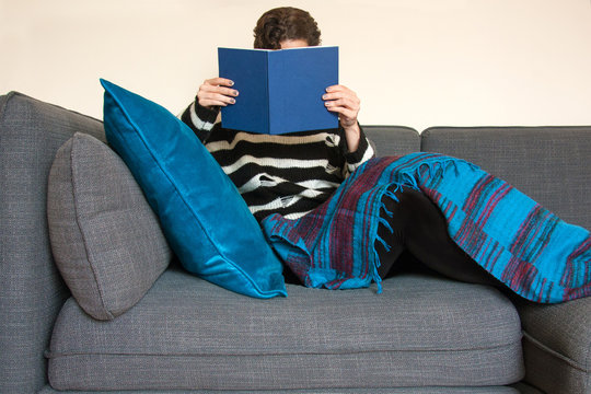 Young woman reading a book, relaxing on a sofa