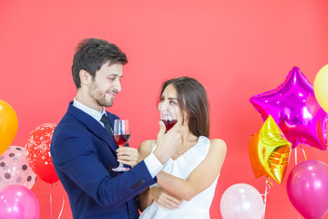 The romantic couple holds in hand wine glass with happiness face celebrating a new year party on a red background and air balloons. Happy New Year and Merry x mas, Valentine, Woman day concept.
