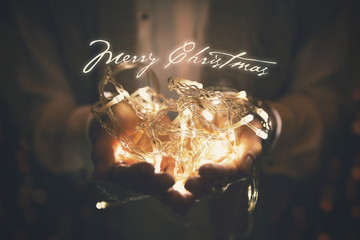 merry christmas greeting card - led lights garland glowing in woman hands