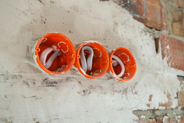 Socket orange boxes with wires in a wall. Cabling installation of electrical wires sticking out from electrical sockets hole on brick wall.