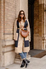 street style portrait of an attractive woman wearing a beige trench coat, denim jeans, black ankle boots and brown leather bag, crossing the street. fashion outfit perfect for autumn fall winter © mlasaimages