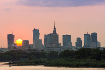 Fototapeta Panorama wieżowców w Warszawie podczas kolorowego zachodu słońca, odbicie w Wiśle, Polska obraz