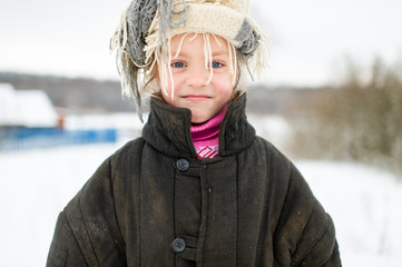 Emotional portrait of positive slavonic girl wearing loose fit padded jacket with scarf on her head in winter snowy day in village