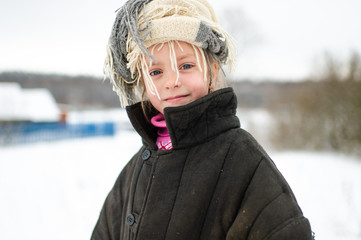 Emotional portrait of positive slavonic girl wearing loose fit padded jacket with scarf on her head in winter snowy day in village